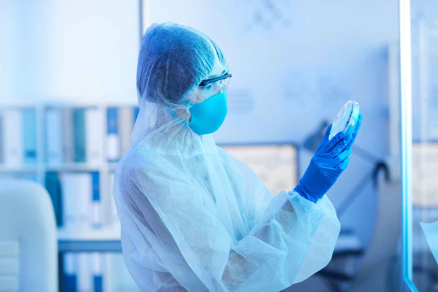 Labormitarbeiterin in Schutzanzug begutachtet Petrischale